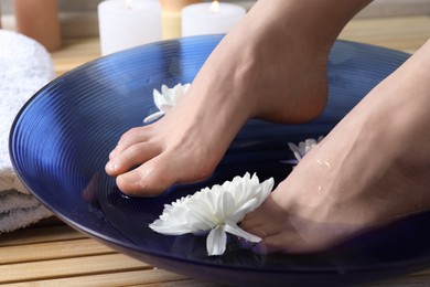 Photo of Woman soaking her feet in bowl with water and flowers on floor, closeup. Spa treatment