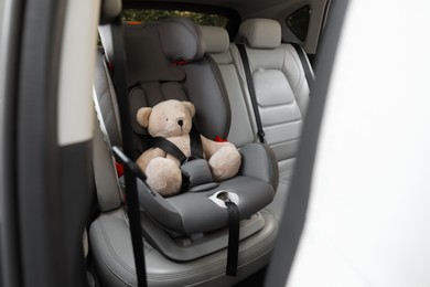 Teddy bear fastened with car safety belt in child seat