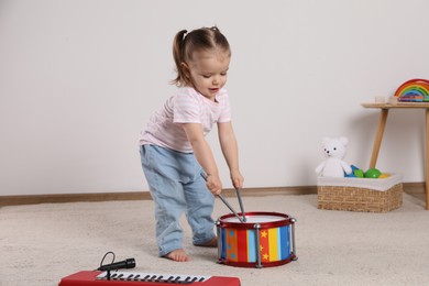 Cute little girl playing with drum, drumsticks and toy piano at home