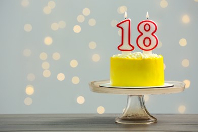 Coming of age party - 18th birthday. Delicious cake with number shaped candles on wooden table against blurred lights, space for text