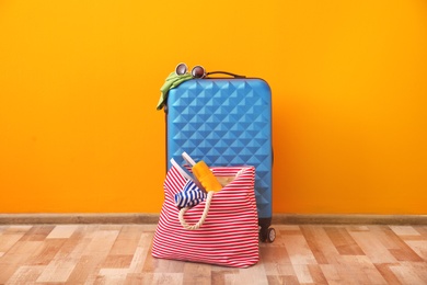 Photo of Suitcase and bag packed for summer journey on floor near color wall