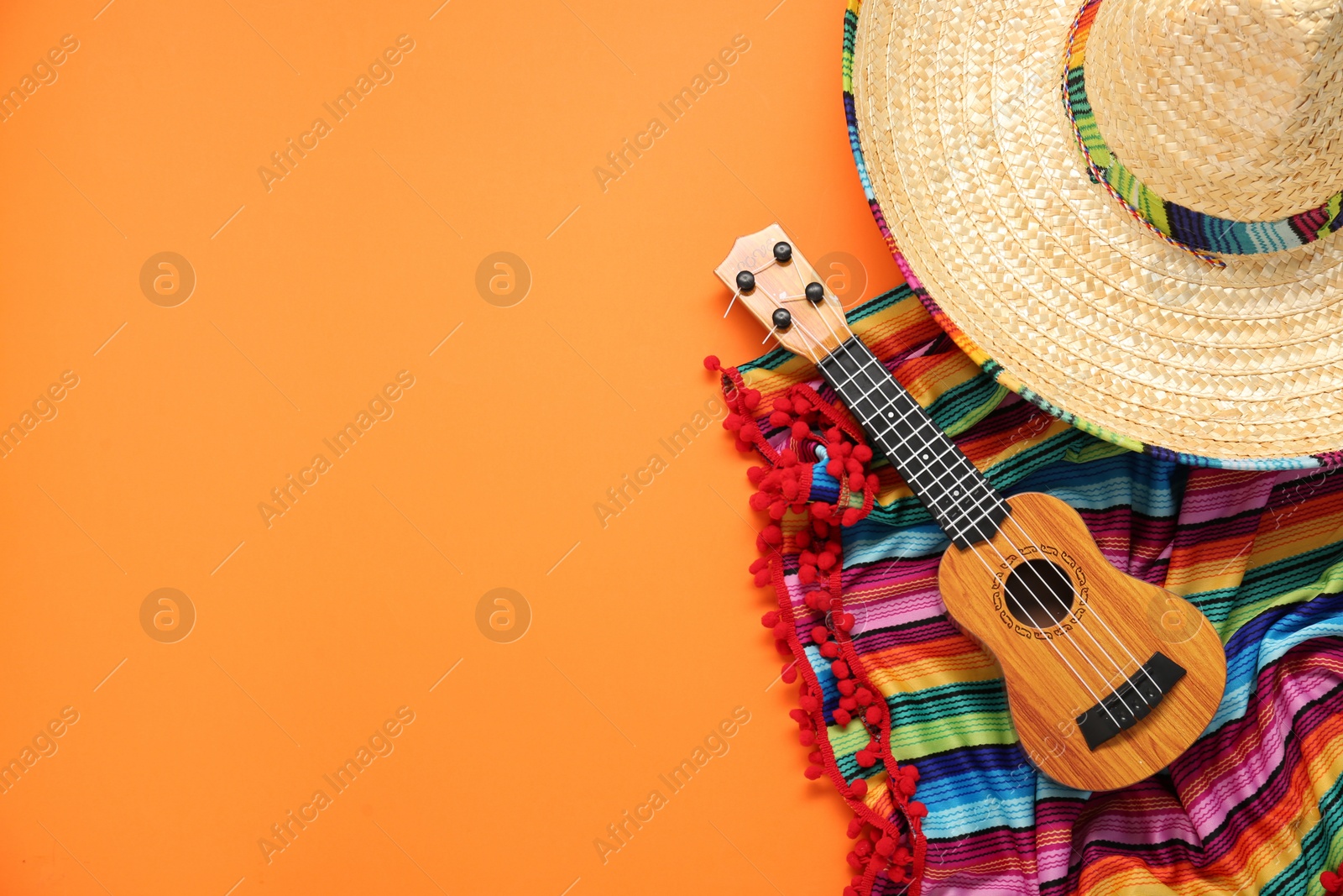 Photo of Mexican sombrero hat, guitar and colorful poncho on orange background, flat lay. Space for text