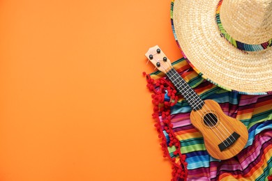 Photo of Mexican sombrero hat, guitar and colorful poncho on orange background, flat lay. Space for text