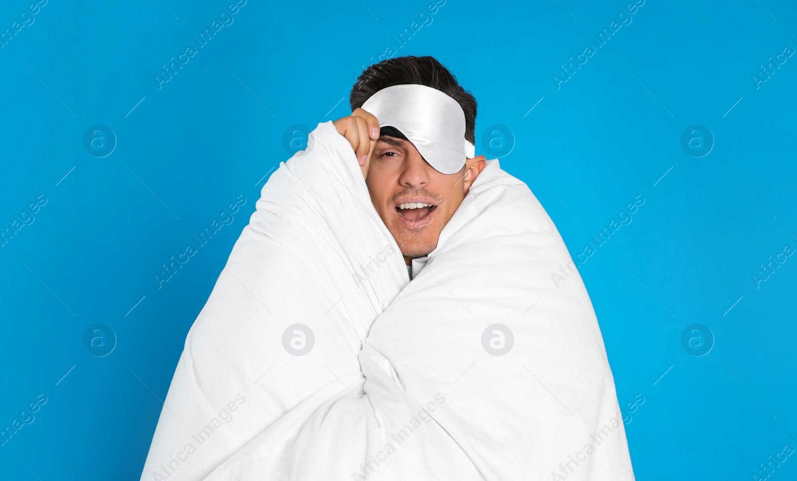 Photo of Man wrapped in blanket wearing sleeping mask on blue background