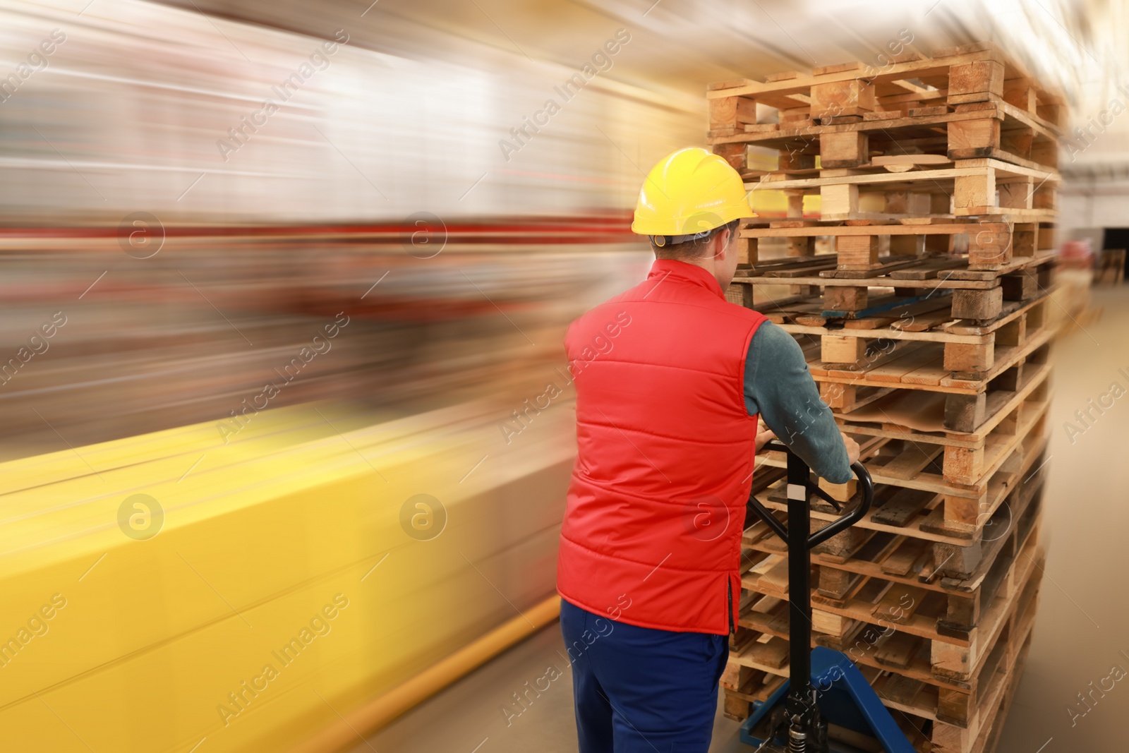 Image of Worker moving wooden pallets with manual forklift in warehouse, back view