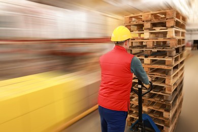 Worker moving wooden pallets with manual forklift in warehouse, back view