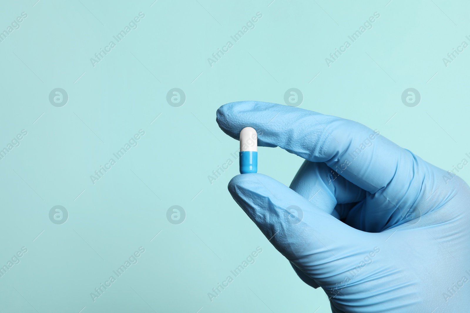 Photo of Doctor holding pill on turquoise background, closeup. Space for text