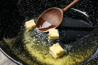 Photo of Frying pan with melting butter and wooden spoon, closeup