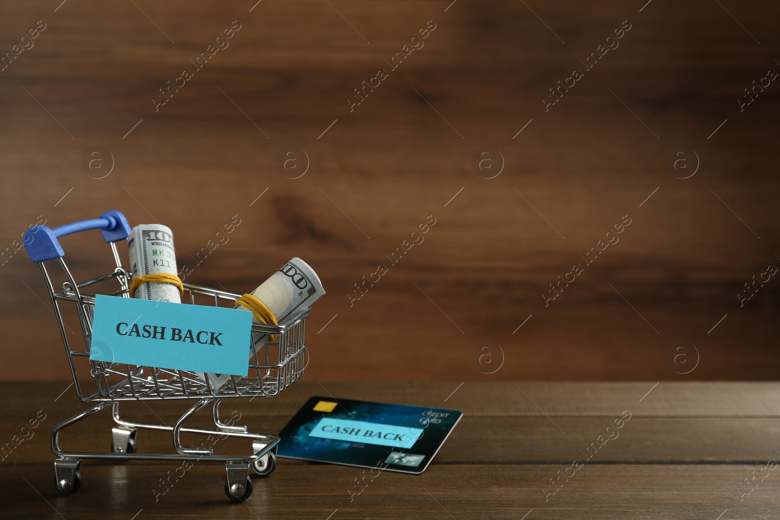 Photo of Credit card and small shopping cart with signs Cash Back on wooden table. Space for text