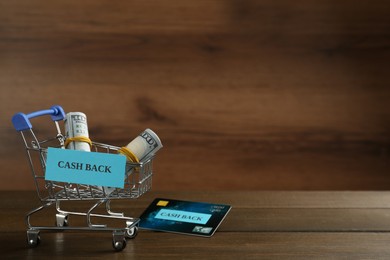 Photo of Credit card and small shopping cart with signs Cash Back on wooden table. Space for text