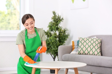 Photo of Young woman cleaning table with rag indoors