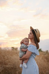 Happy mother with adorable baby in field at sunset