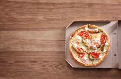 Cardboard box with tasty pizza on wooden background, top view with space for text