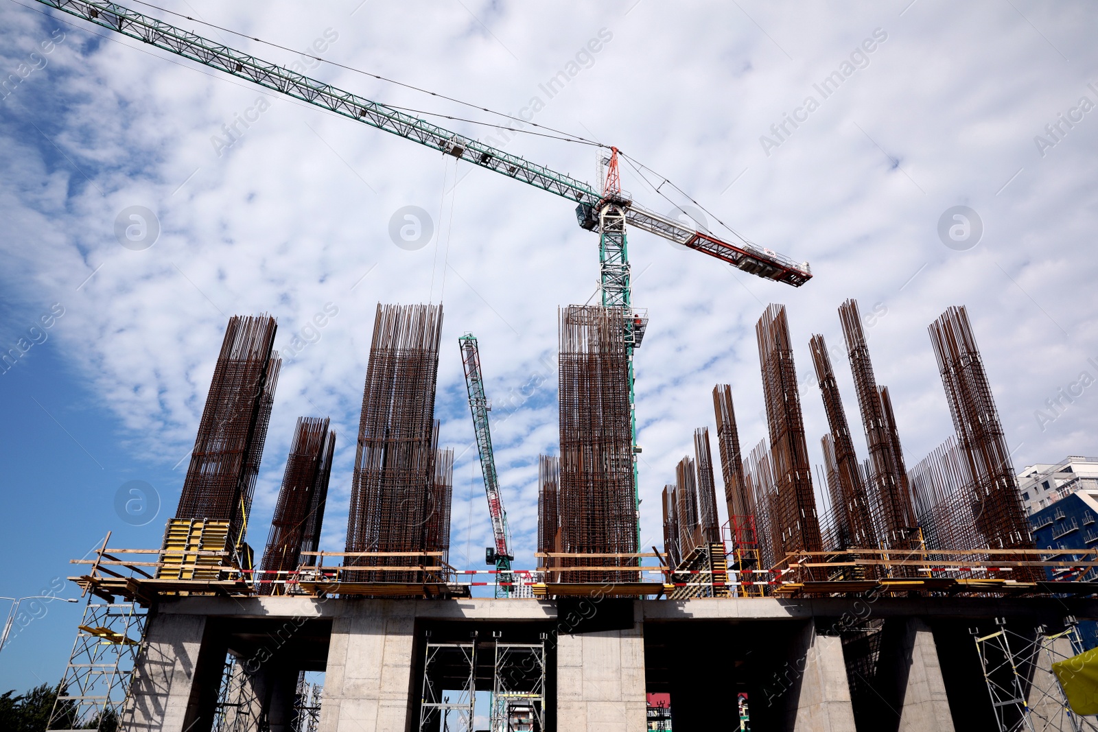 Photo of Tower crane near building under construction against cloudy sky