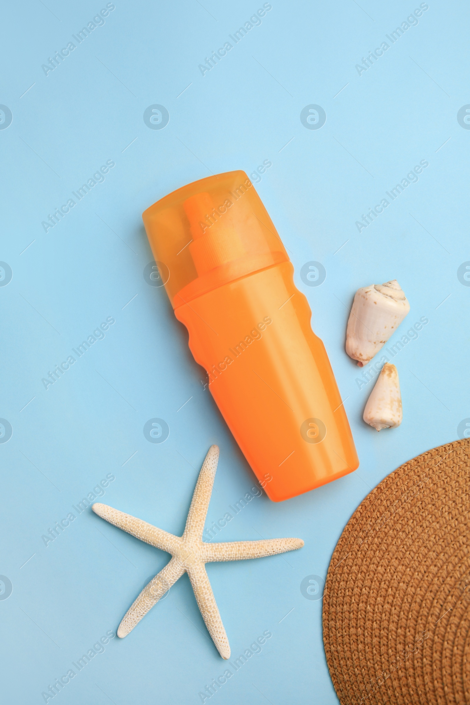 Photo of Bottle of sunscreen, starfish and seashells on light blue background, flat lay