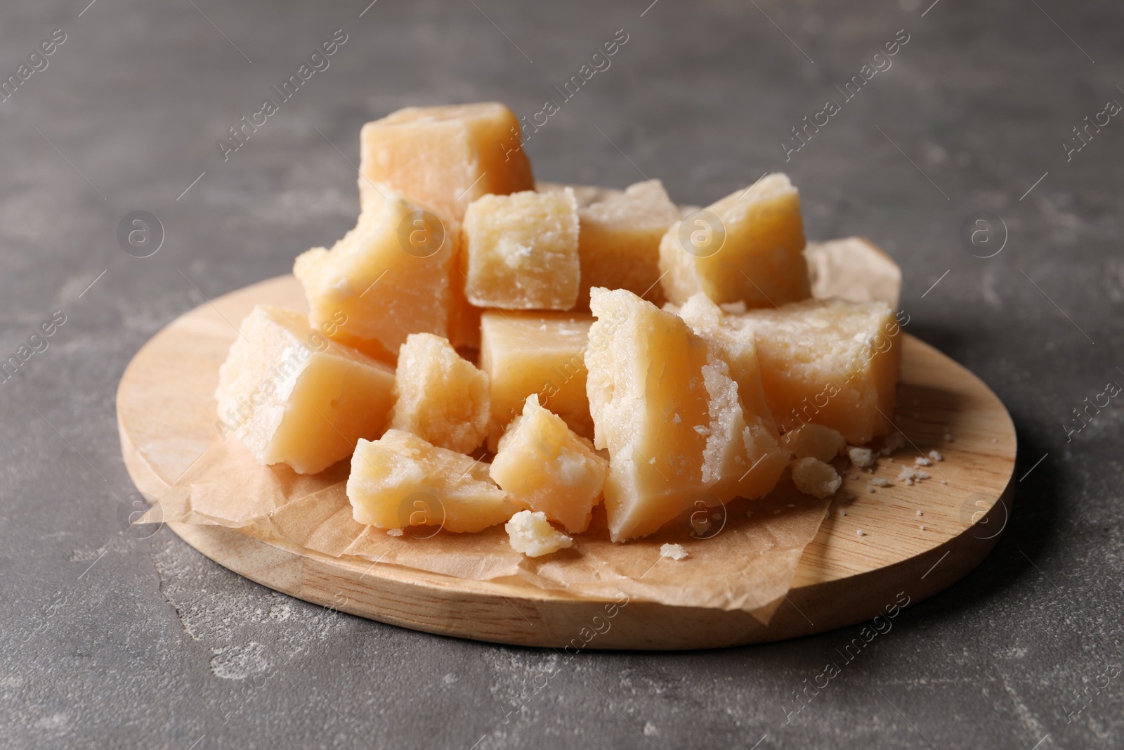 Photo of Parmesan cheese with wooden board on grey table, closeup