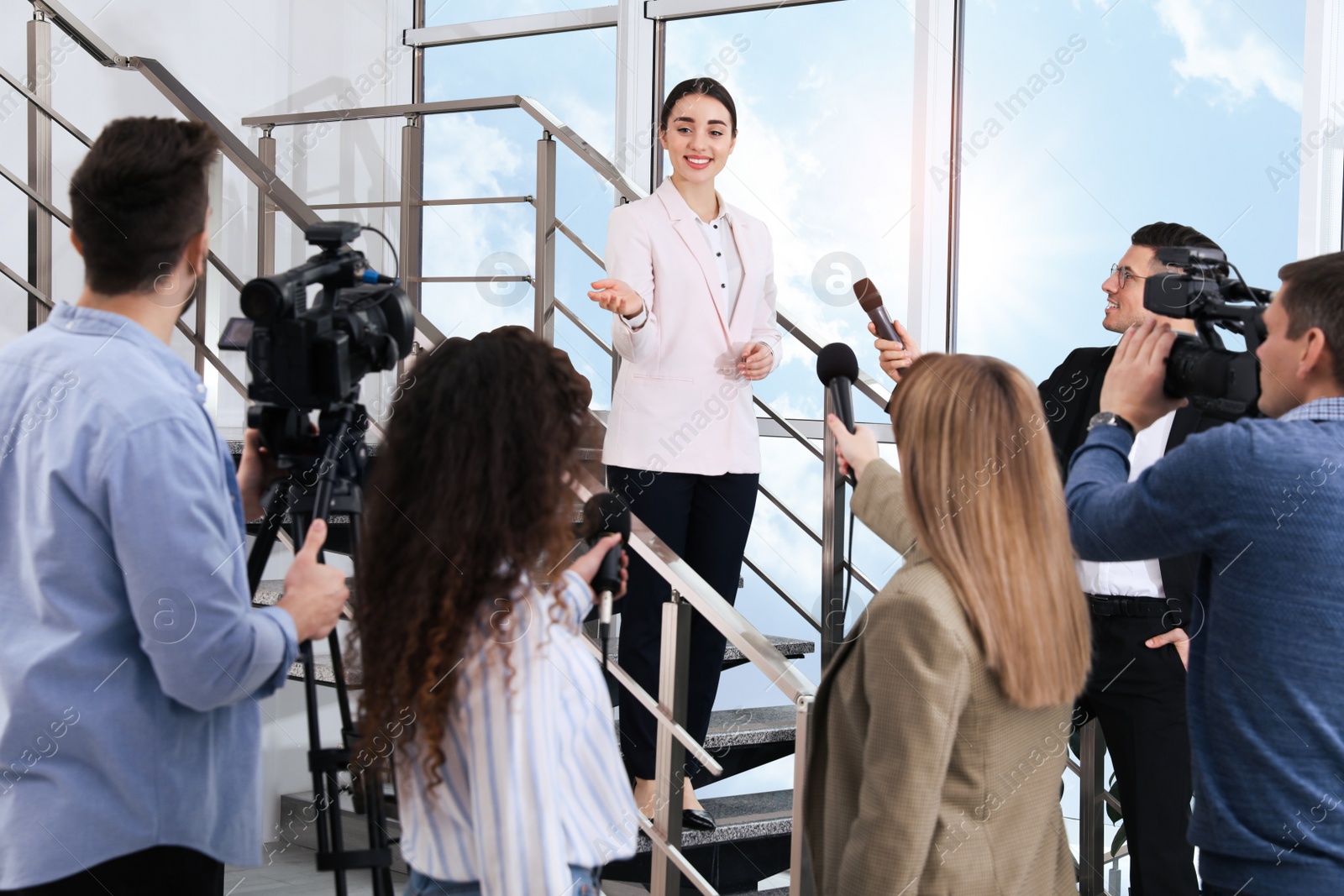 Photo of Happy business woman talking to group of journalists indoors