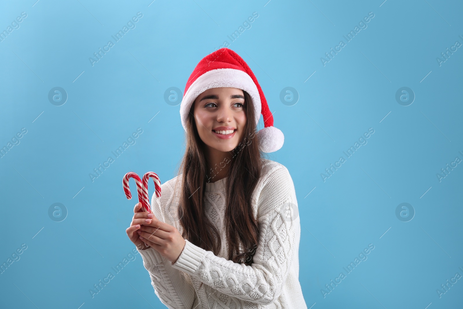 Photo of Beautiful woman in Santa Claus hat holding candy canes on light blue background