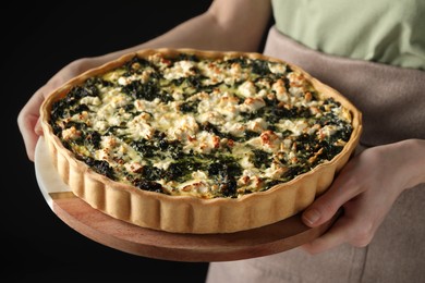 Woman holding delicious homemade spinach quiche on dark background, closeup