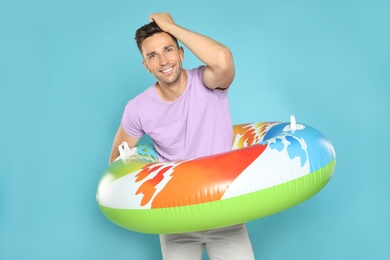 Happy young man with bright inflatable ring on blue background
