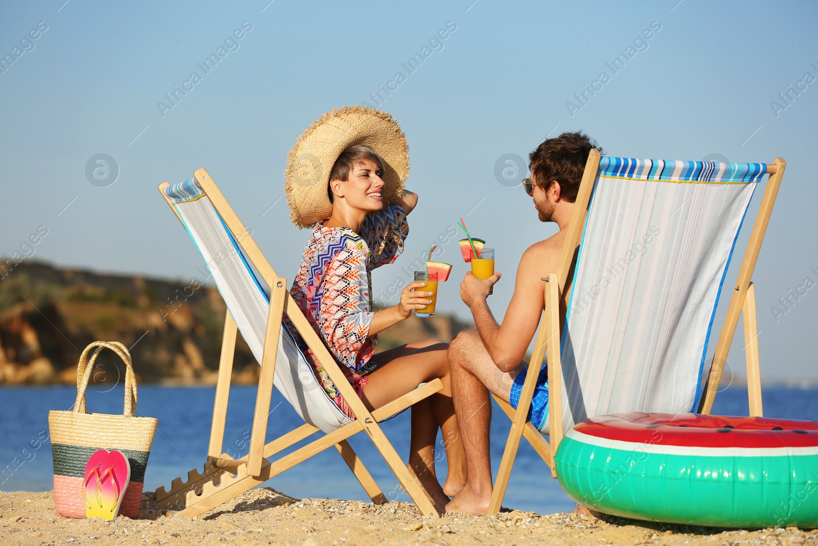 Photo of Young couple with cocktails in beach chairs at seacoast