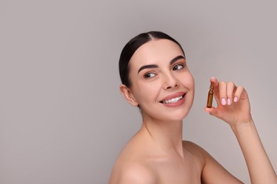 Photo of Beautiful young woman holding skincare ampoule on grey background. Space for text