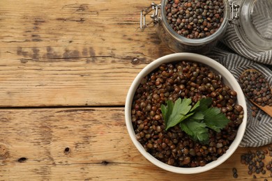 Photo of Bowl of delicious lentils, jar and spoon with raw seeds on wooden table, top view. Space for text