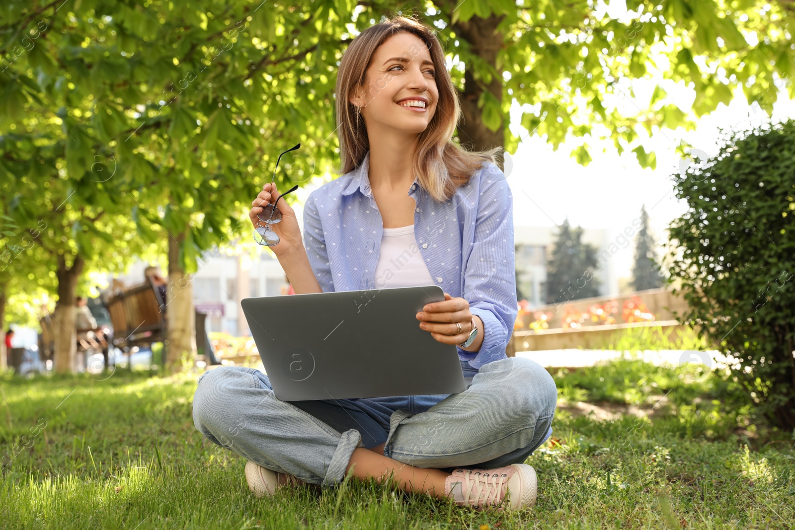 Image of Happy young woman with laptop sitting on green grass in park