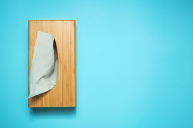 Photo of Wooden holder with paper tissues on light blue background, top view. Space for text