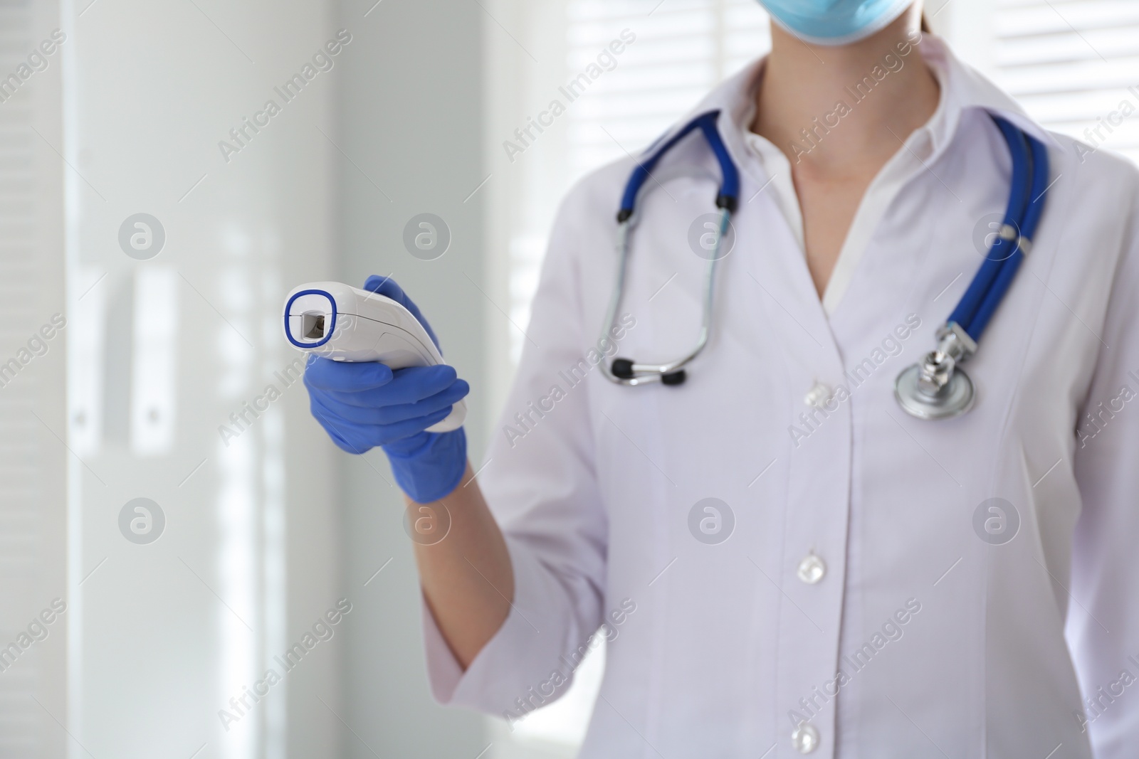 Photo of Doctor holding non contact infrared thermometer indoors, closeup. Measuring temperature