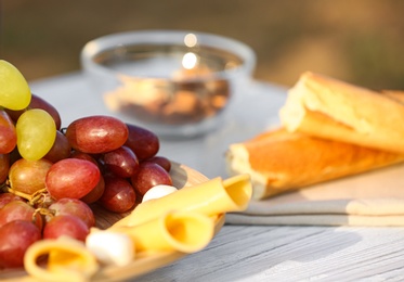 Plate with cheese and grapes on white wooden table outdoors, closeup view