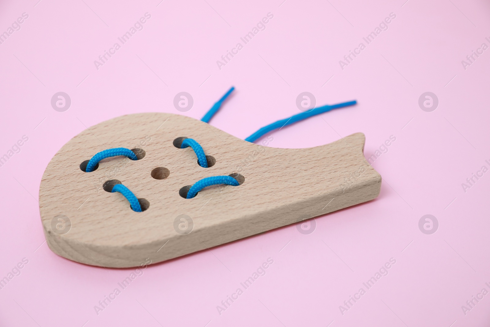 Photo of Wooden whale figure with holes and lace on pink background. Educational toy for motor skills development