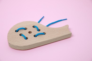 Photo of Wooden whale figure with holes and lace on pink background. Educational toy for motor skills development