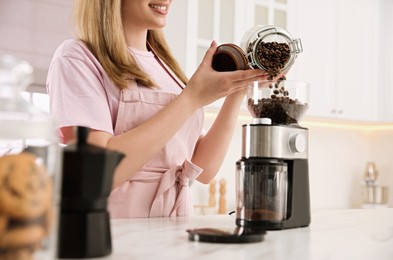 Photo of Woman using electric coffee grinder in kitchen, closeup