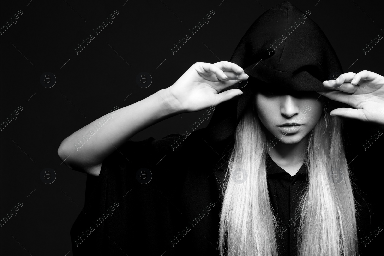 Photo of Witch in mantle on dark background, black and white effect. Scary fantasy character