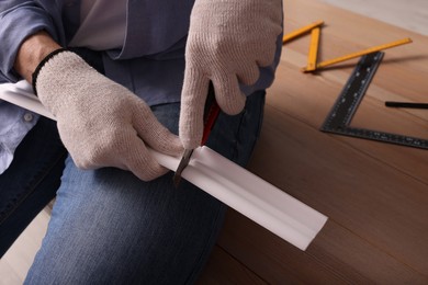 Man cutting foam crown molding with utility knife near wooden table, closeup