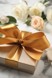 Photo of Golden gift box and beautiful roses on white marble table, closeup