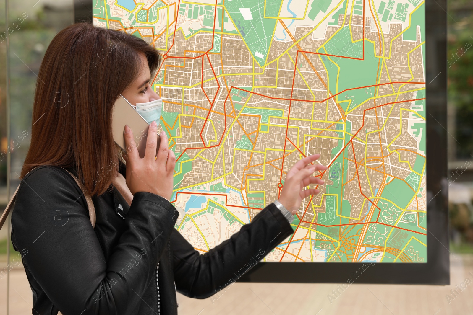 Image of Young woman in medical face mask talking on phone near public transport map at bus stop