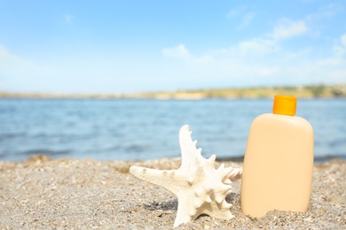 Photo of Bottle of sun protection body cream and starfish on beach, space for design