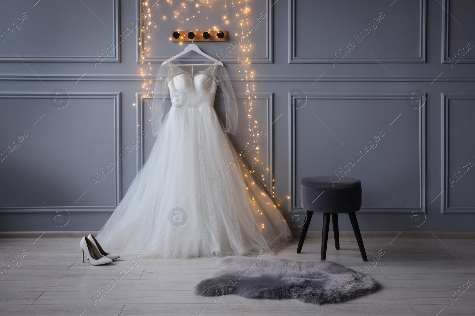 Photo of Fashionable long dress with transparent sleeves on hanger near festive lights and shoes in showroom. Preparing for party