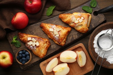 Photo of Fresh tasty puff pastry with sugar powder, mint, blueberries and apples served on wooden table, flat lay