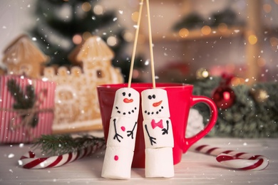 Photo of Funny snowmen made of marshmallows near cup with hot drink on white wooden table