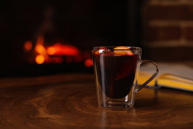 Photo of Tasty mulled wine and blurred fireplace on background