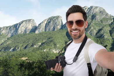 Smiling man with camera taking selfie in mountains