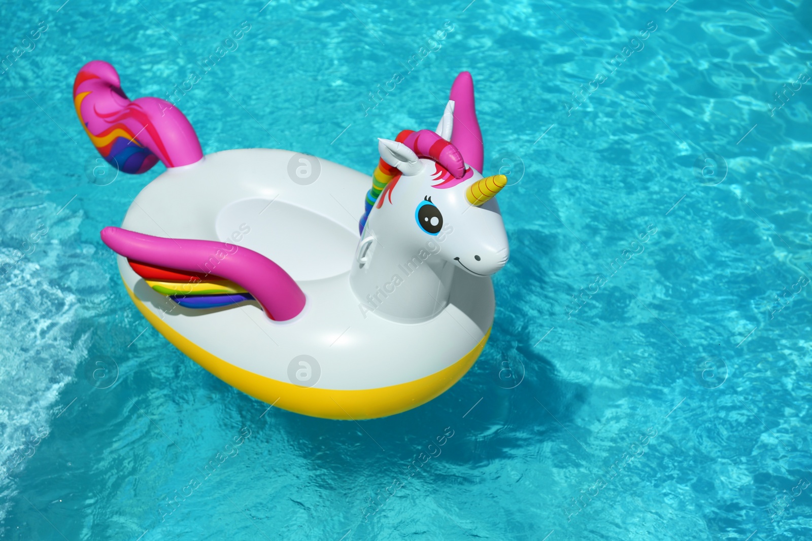 Photo of Funny inflatable unicorn ring floating in swimming pool on sunny day. Space for text