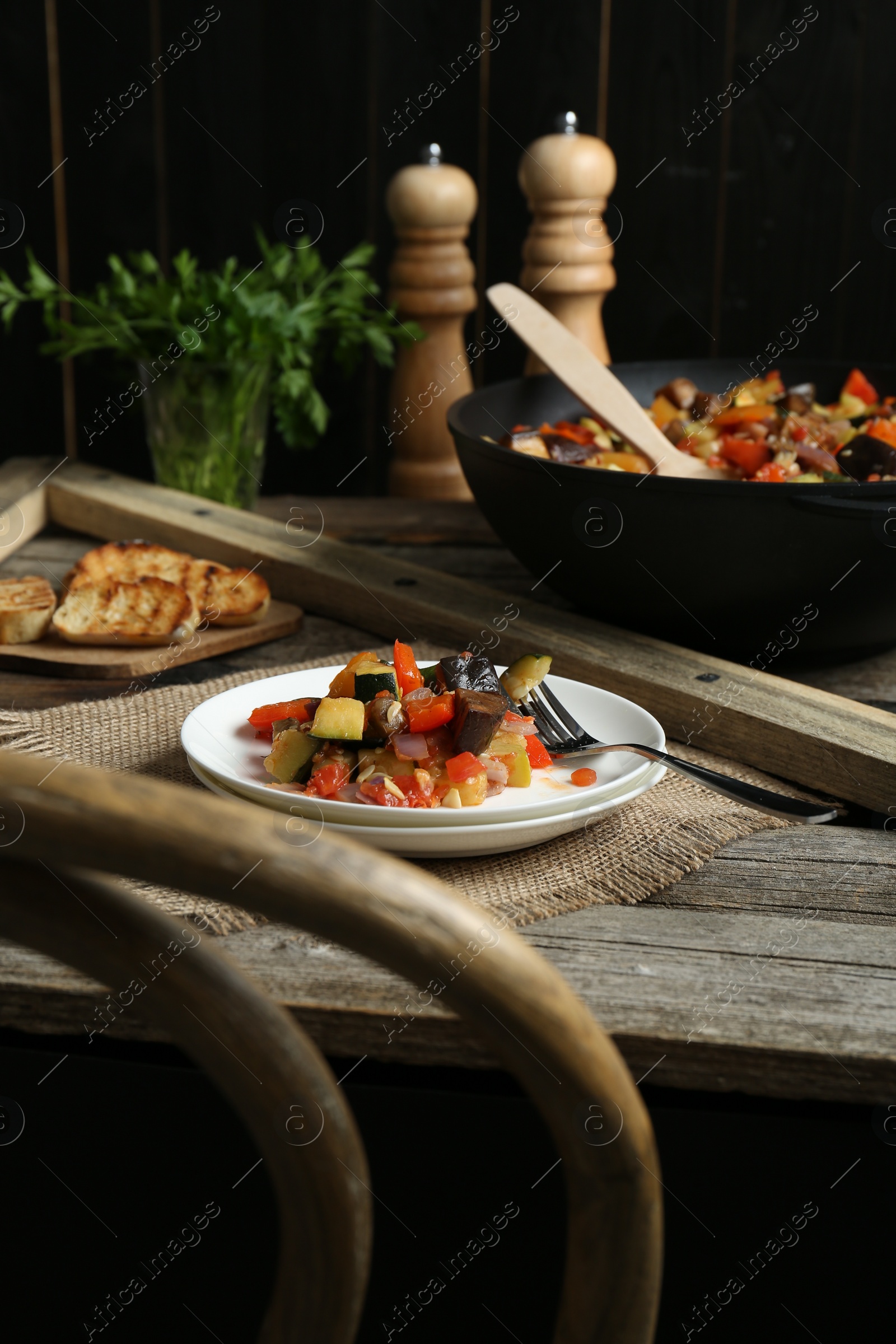 Photo of Delicious ratatouille served with bread on wooden table