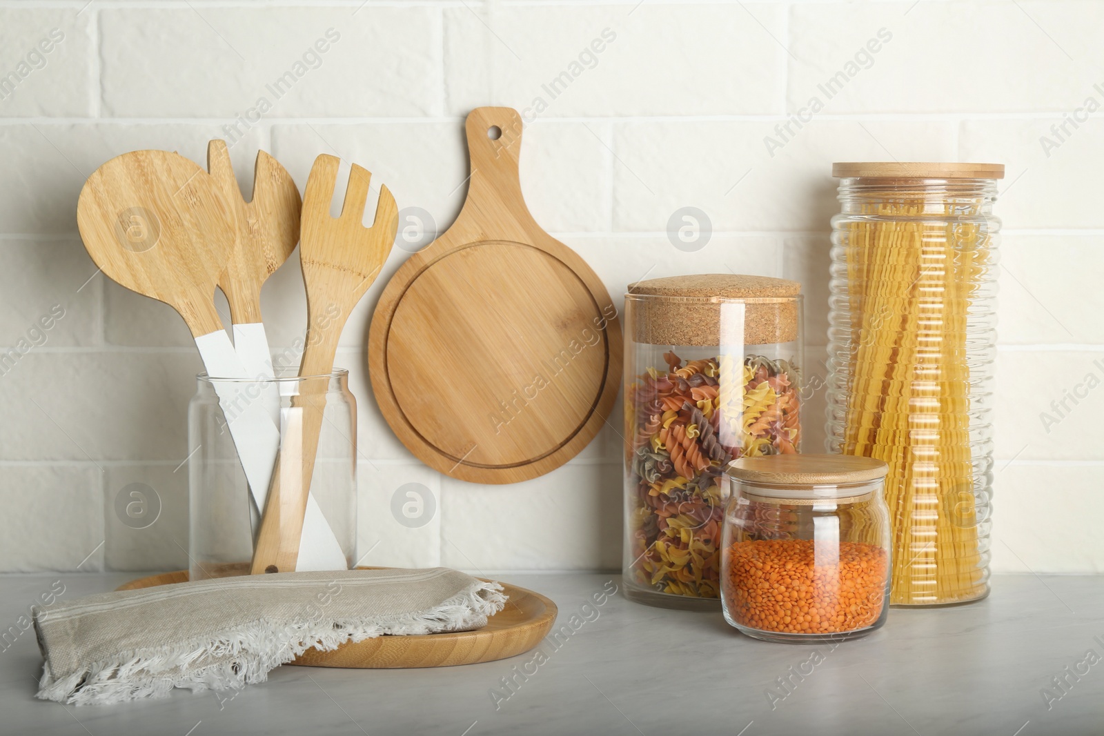 Photo of Wooden utensils and different products on grey table near white brick wall in kitchen