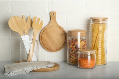 Photo of Wooden utensils and different products on grey table near white brick wall in kitchen