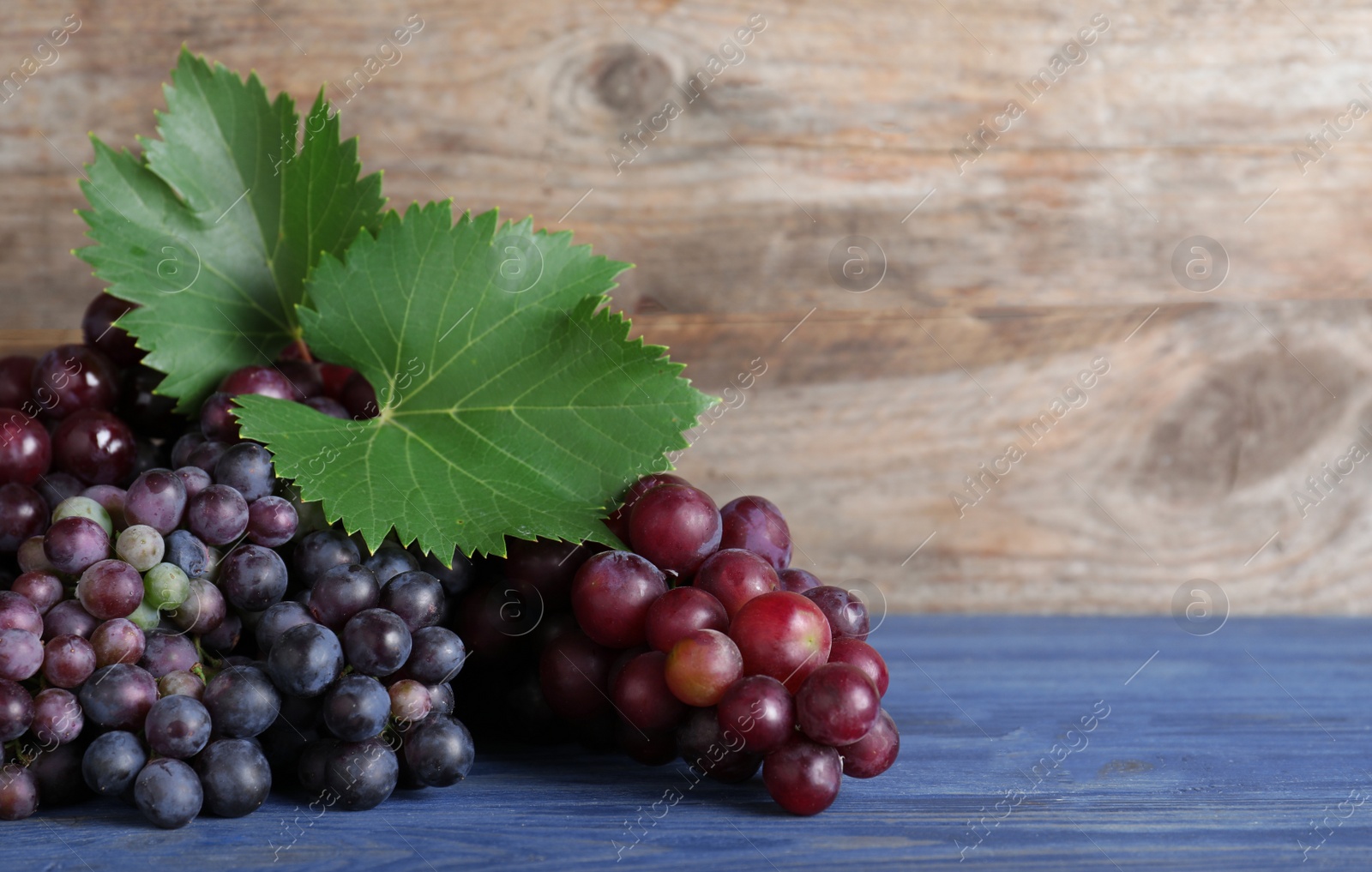 Photo of Fresh ripe juicy grapes on blue table against wooden background. Space for text