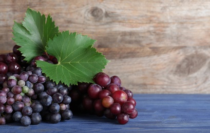 Photo of Fresh ripe juicy grapes on blue table against wooden background. Space for text